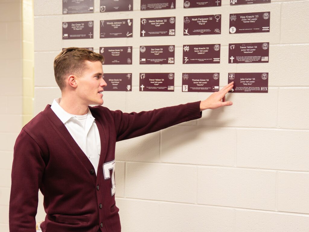 Yell leader in maroon sweater pointing at name plate