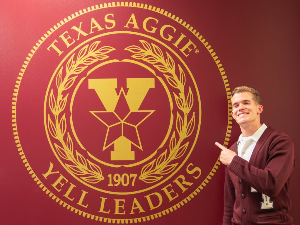 Yell leader standing in front of Texas Aggie Yell Leaders seal