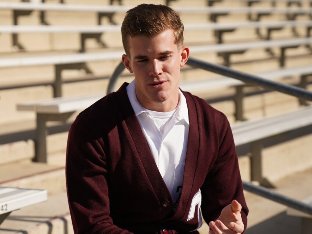 Yell leader in maroon sweater sitting in stadium seating