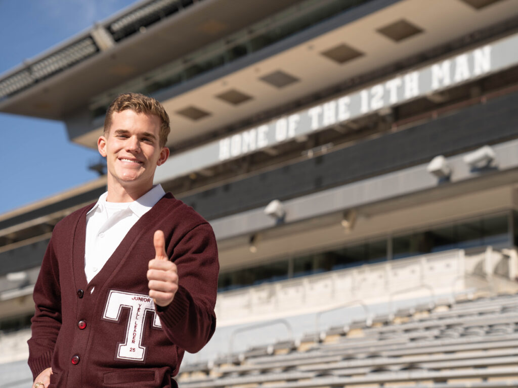 Yell leader in maroon sweater giving a thumbs up in Texas A&M football stadium