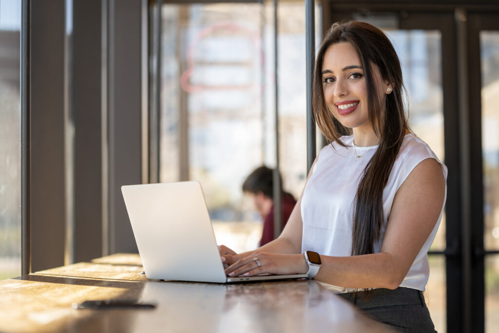 Girl in business attire using a laptop and smiling at the camera