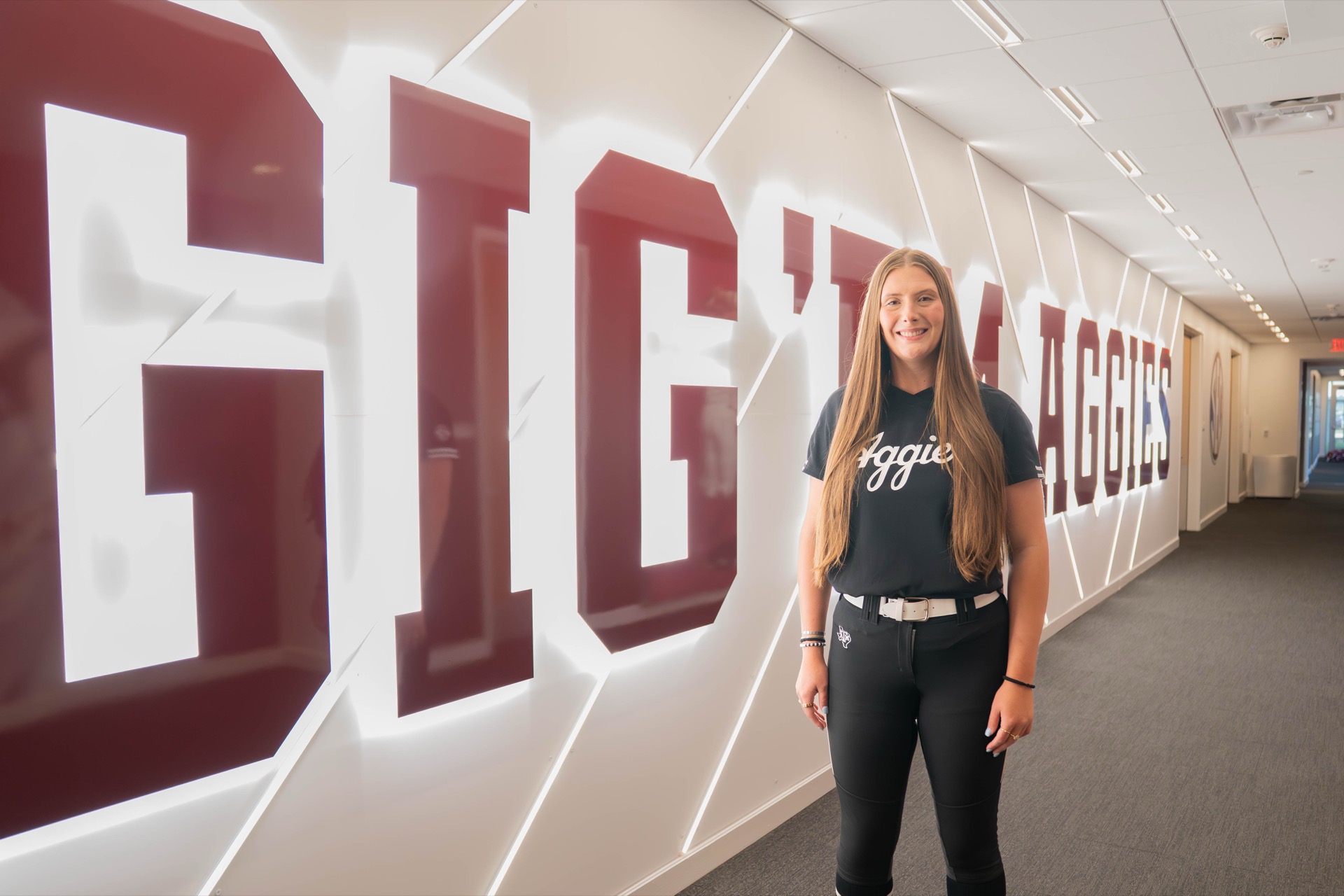 Emiley Kennedy with her softball jersey in front of Gig'em Aggies sign