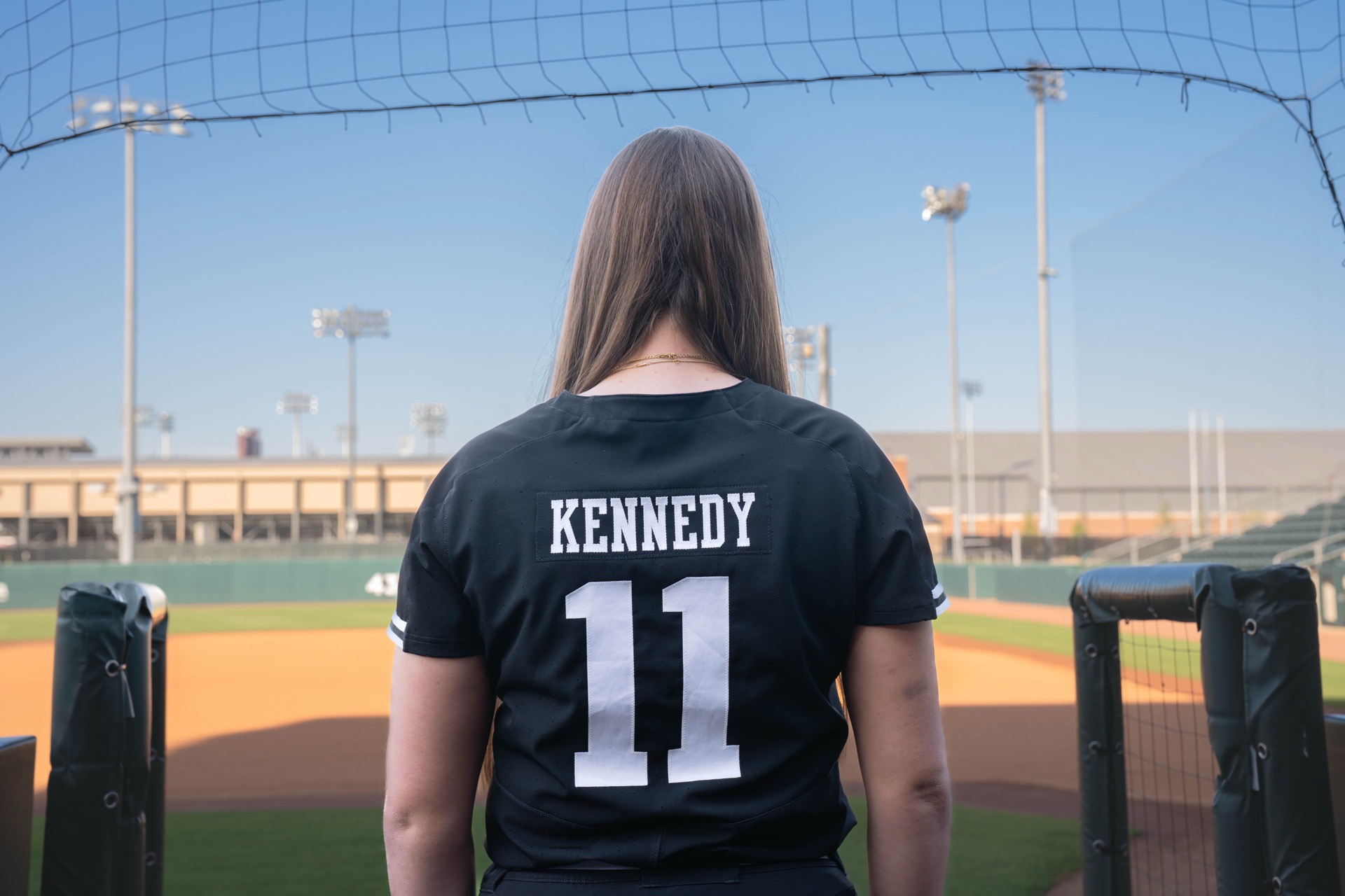 Emiley Kennedy's at the softball field, facing back with her softball jersey with showing "Kennedy 11"