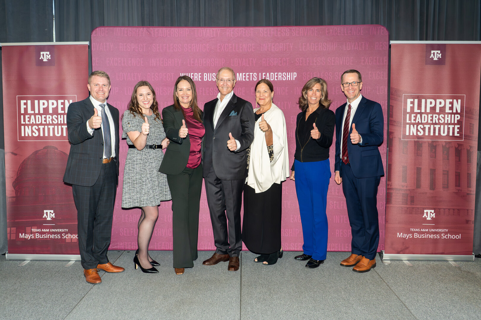 A group poses in front of a maroon backdrop